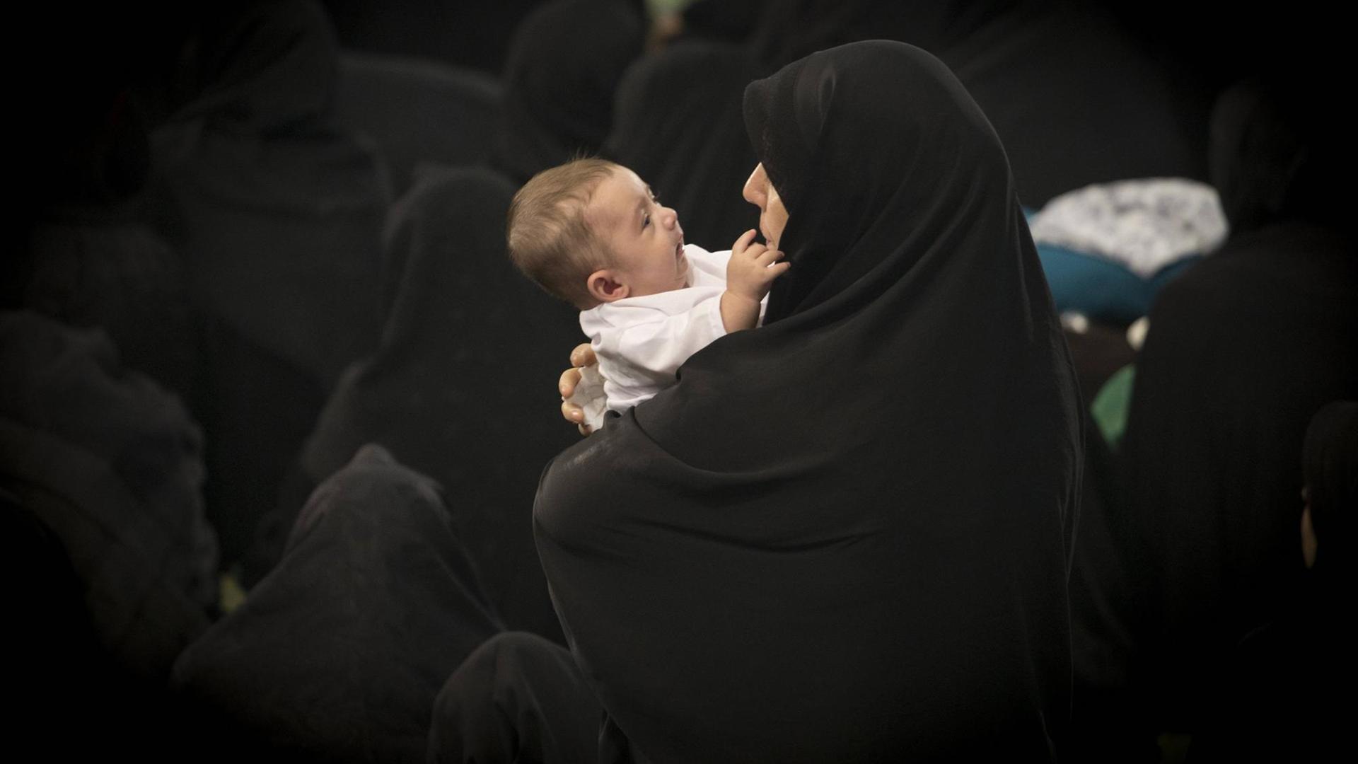 Eine iranische Mutter im schwarzen Tschador hält ihr Baby im Arm, Teheran.