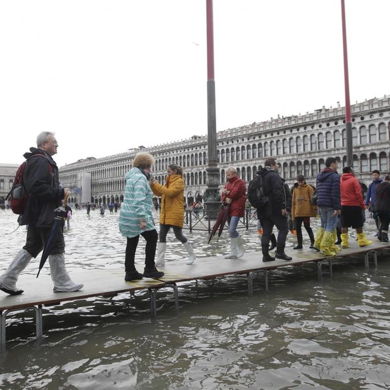 Touristen gehen auf einem improvisierten Holzsteg über den überfluteten Markusplatz (1.11.2018).