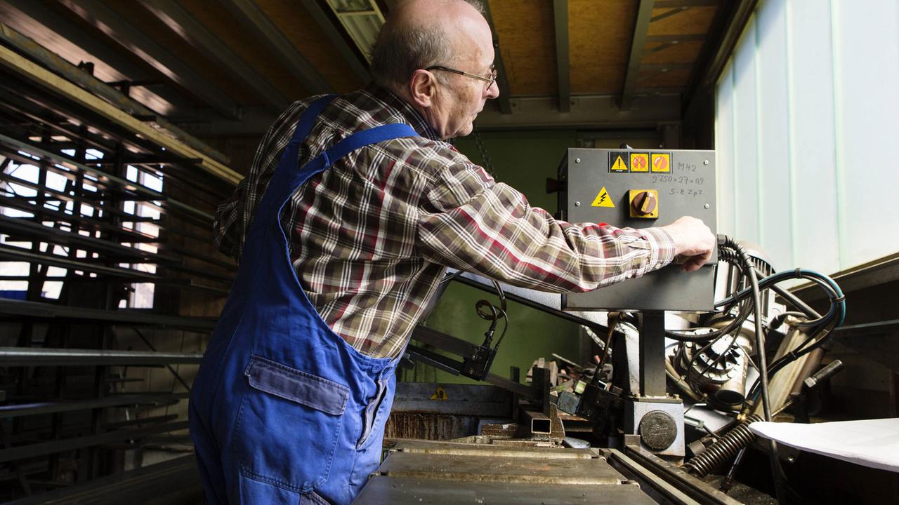 Ein älterer Mann in kariertem Hemd und blauer Arbeitshose bedient eine Maschine in einem mittelständischem Unternehmen