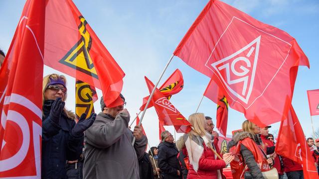 Teilnehmer eines Warnstreiks halten rote Fahnen mit dem Logo der Gewerkschaft IG Metall