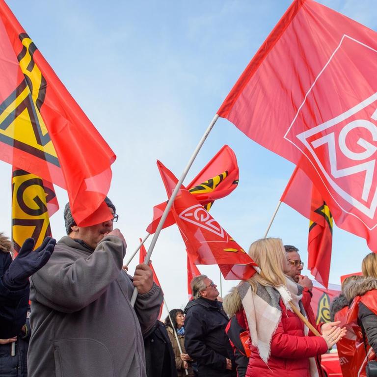 Teilnehmer eines Warnstreiks halten rote Fahnen mit dem Logo der Gewerkschaft IG Metall
