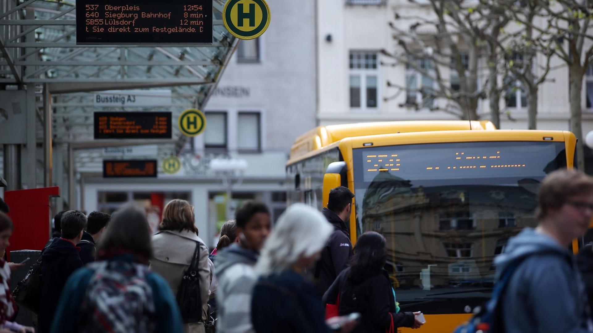Menschen warten an einer Bushaltestelle in Bonn.