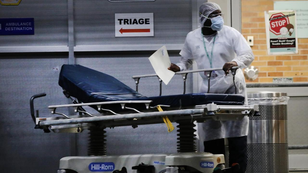 Maimonides Medical Center in New York: Ein Mitarbeiter in Schutzkleidung steht mit einem mobilen Krankenbett vor einem Schild mit der Aufschrift "Triage".