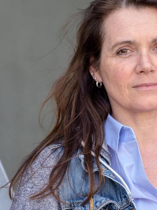 Barbara Junge steht in legerer Kleidung und mit ernstem Blick vor einer Metallkonstruktion.