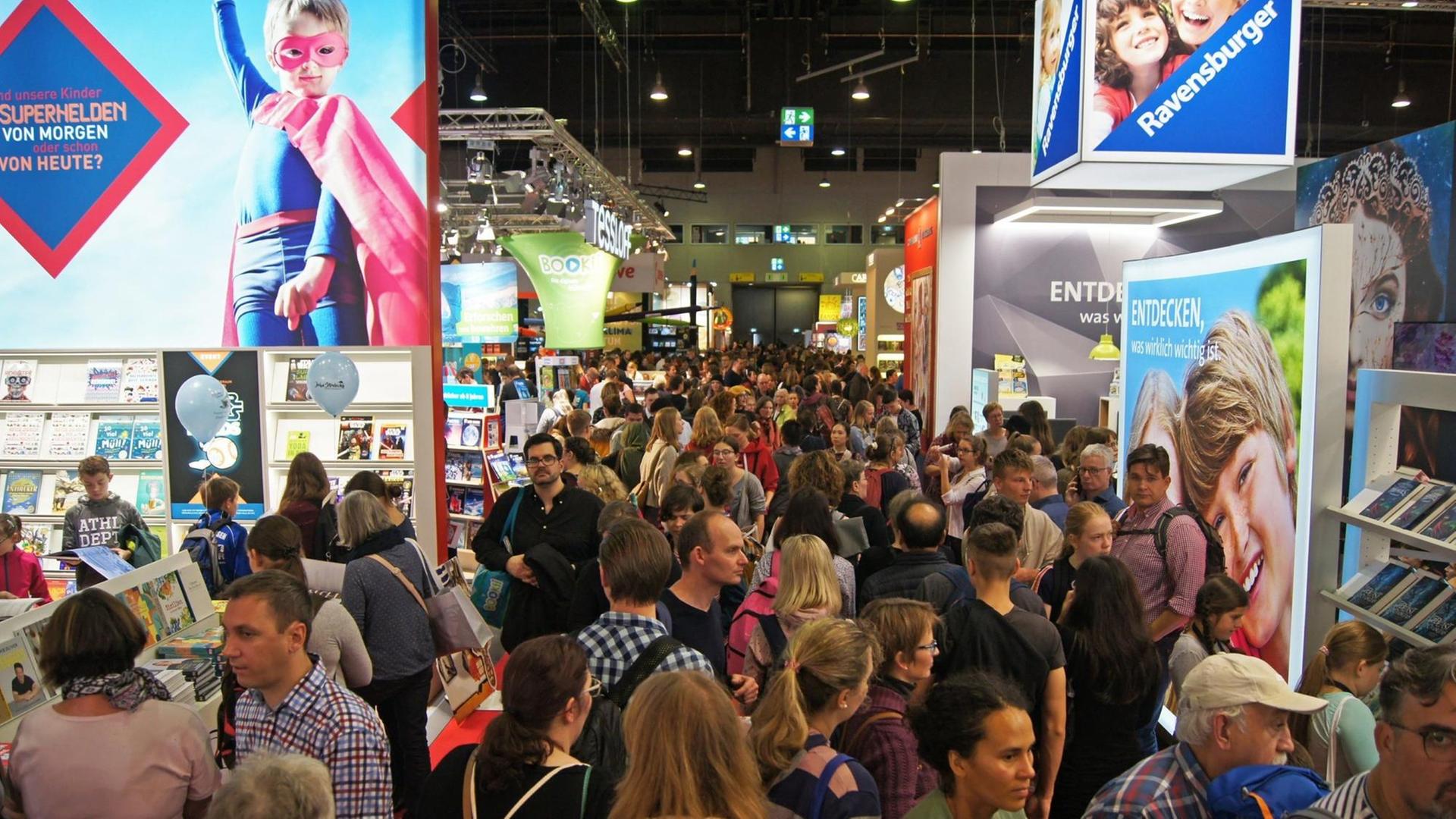 Blick in eine Ausstellungshalle der Frankfurter Buchmesse 2019, die Gänge sind voller Menschen, die zwischen den Ständen der Verlagen laufen und diese betrachten.