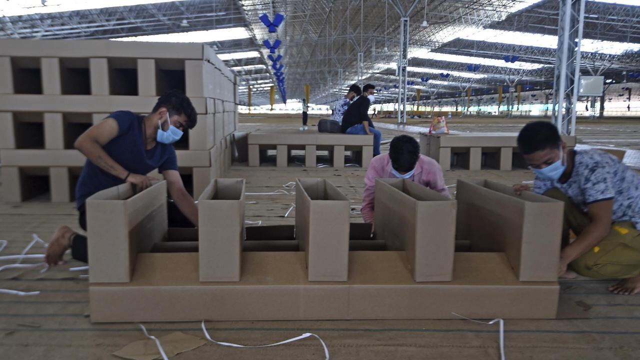 In einer Halle setzen drei Männer vorgefertigte Pappteile zusammen, um daraus eine Liege herzustellen.