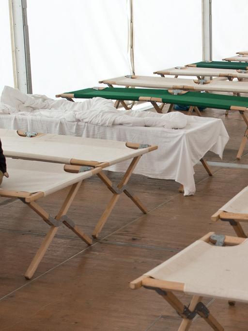 Flüchtlinge sitzen auf Feldbetten in einem Zelt der Hessischen Erstaufnahmeeinrichtung in Gießen.