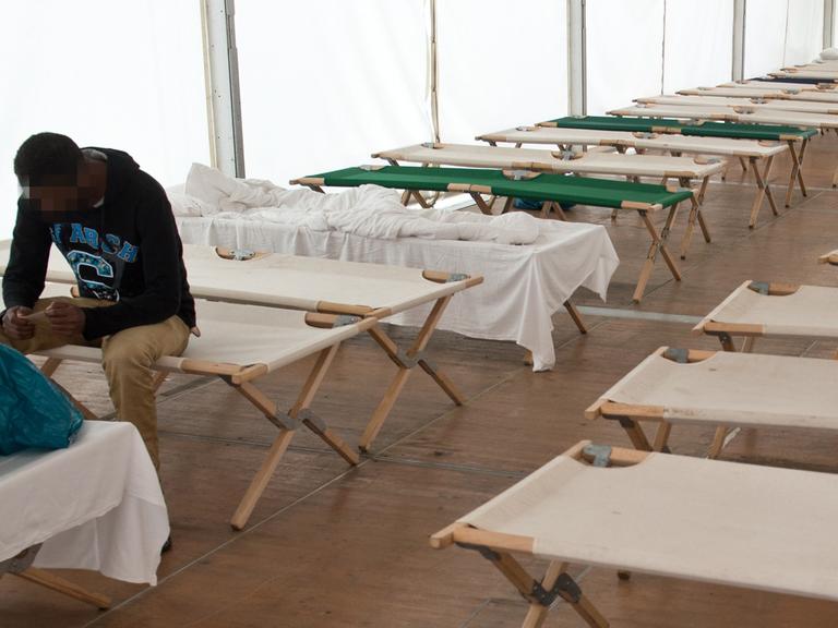 Flüchtlinge sitzen auf Feldbetten in einem Zelt der Hessischen Erstaufnahmeeinrichtung in Gießen.