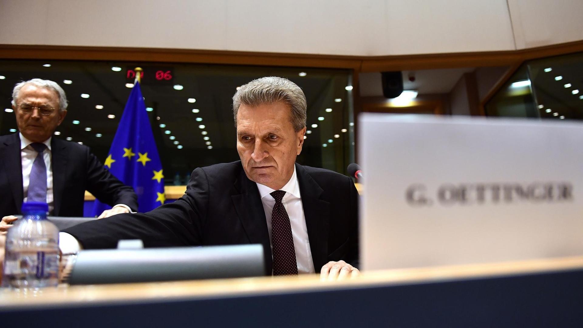 Günther Ottinger stellt sich als neuer EU-Kommissar für Haushalts- und Personalfragen einer Anhörung im Europaparlament. Er sitzt an einem Tisch vor einer Europaflagge. Zu sehen ist im Vordergrund sein Namensschild.