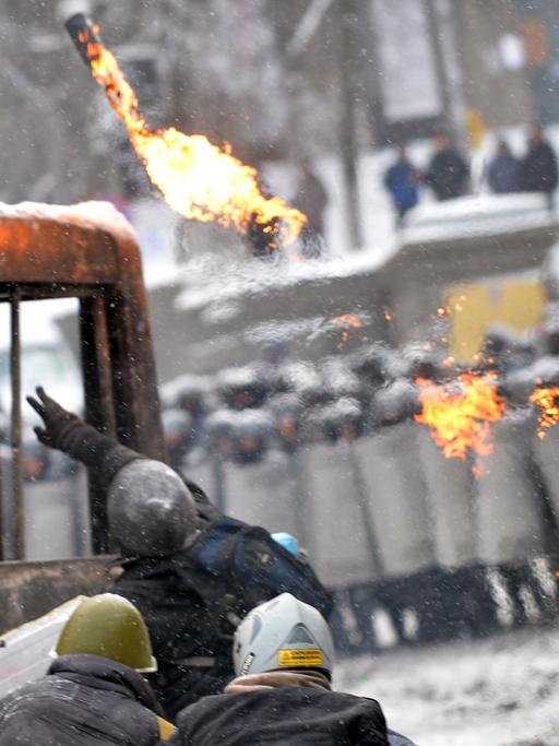 Demonstranten in der Hauptstadt werfen eine Brandbombe auf Polizisten, die Schutzschilder vor sich halten.