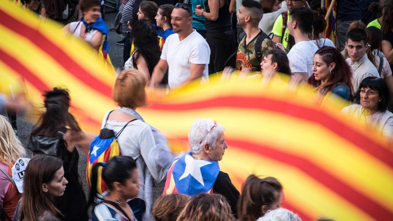 Demonstrationsteilnehmer schütteln ein großes breites Banner in den Farben Kataloniens.