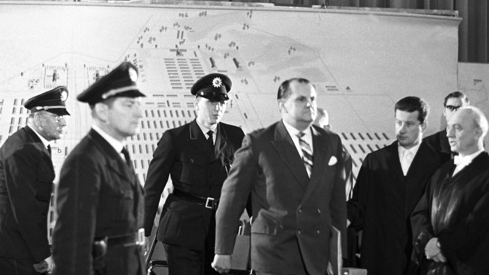 Der Angeklagte Oswald Kaduk wird von drei Polizisten in einen Gerichtssaal geführt.