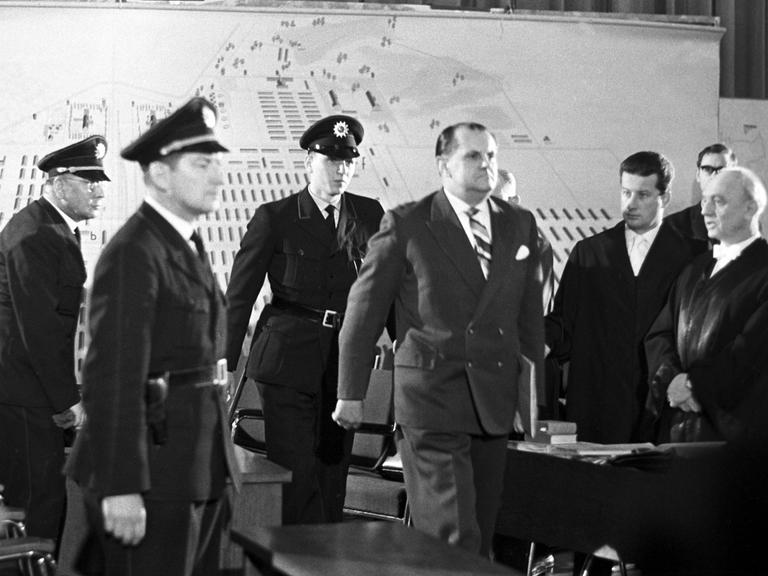 Der Angeklagte Oswald Kaduk wird von drei Polizisten in einen Gerichtssaal geführt.