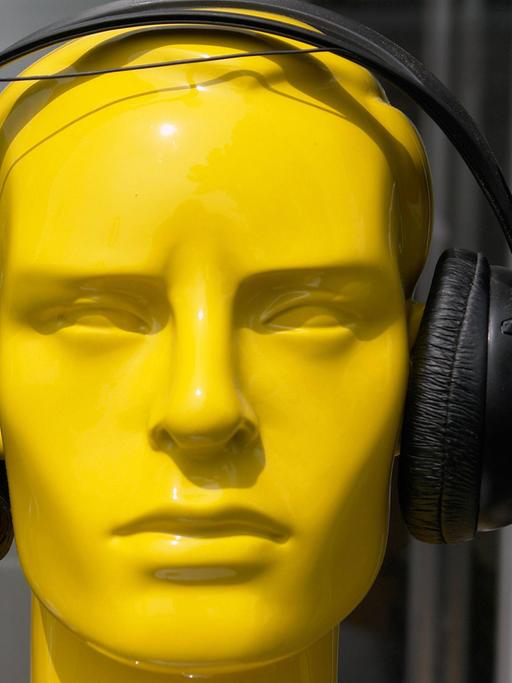 Ein gelber Kunstkopf mit schwarzen Kopfhörern.