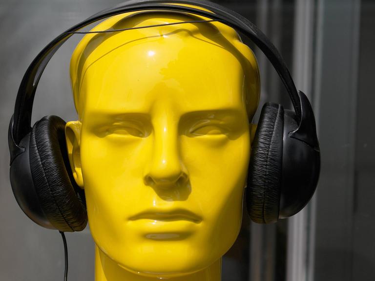 Ein gelber Kunstkopf mit schwarzen Kopfhörern.