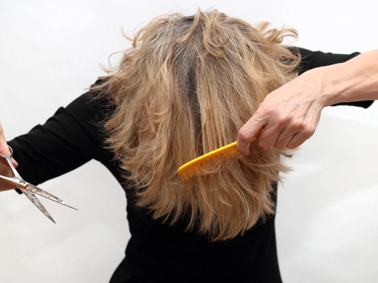 Symbolfoto zeigt ein Person, die sich umständlich versucht selber die Haare zu schneiden.