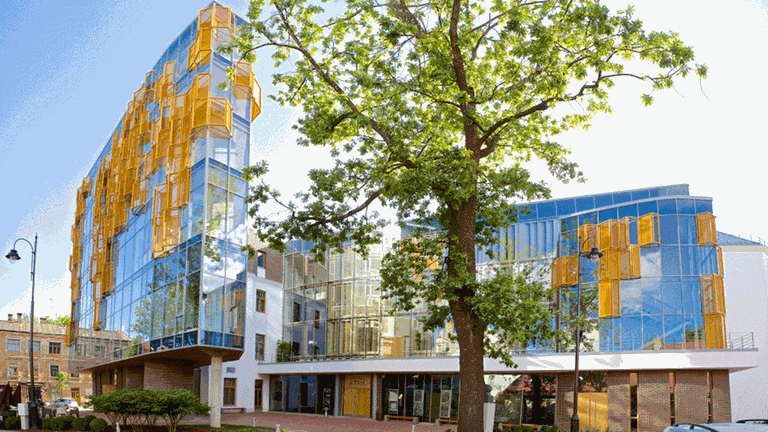 Ein modernes Kultur-Gebäude mit einer farbigen Glasfront, davor steht ein Baum
