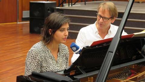 Die Pianistin und der Moderator sitzen am schwarzen Flügel und schauen in die Noten. Der Moderator hält der Pianistin ein Mikrofon zum Hinheinsprechen hin.