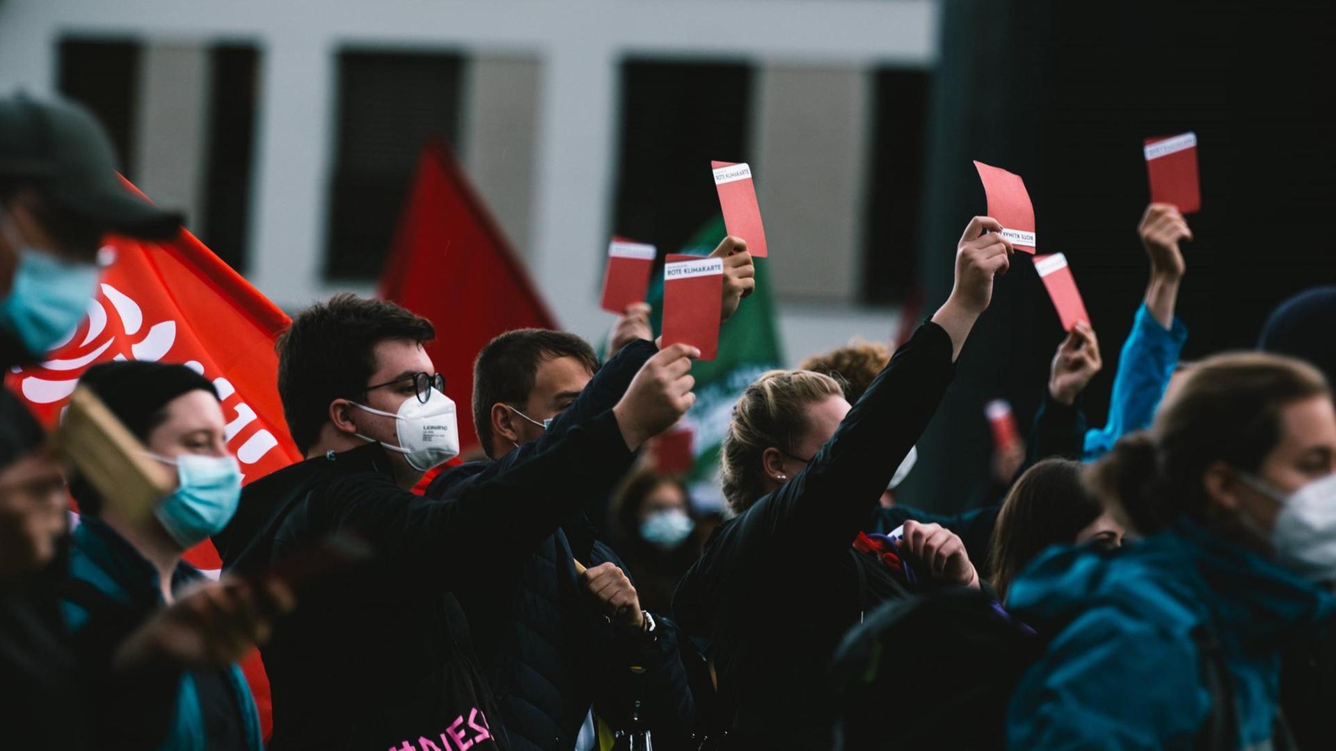 Jugendliche mit Mund-Nasenschutz halten bei einer Demonstration rote Karten hoch, auf denen steht: Rote Klimakarte.