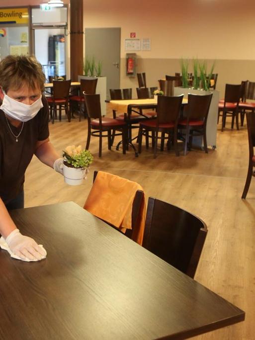 13.05.2020, Sachsen-Anhalt, Wernigerode: Eine Mitarbeiterin mit Mund-Nase-Schutz und einem Reinigungstuch in der Hand beugt sich über einen Restauranttisch.