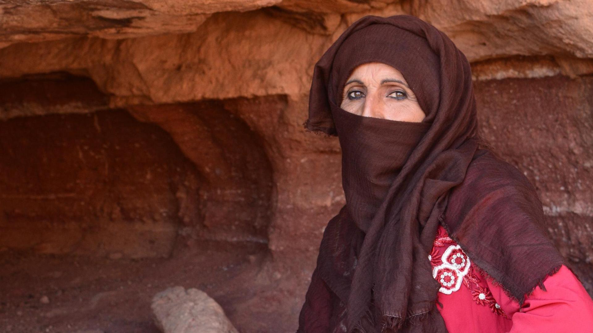Die 48-jährige Wanderführerin Umm Yasser ist in der Höhle hinter ihr aufgewachsen. Durch die Corona-Pandemie kommen derzeit keine Touristen in ihr Tal auf der Sinai-Halbinsel. Sie trägt ein rotes Kleid und ein bräunliches Tuch um den Kopf.