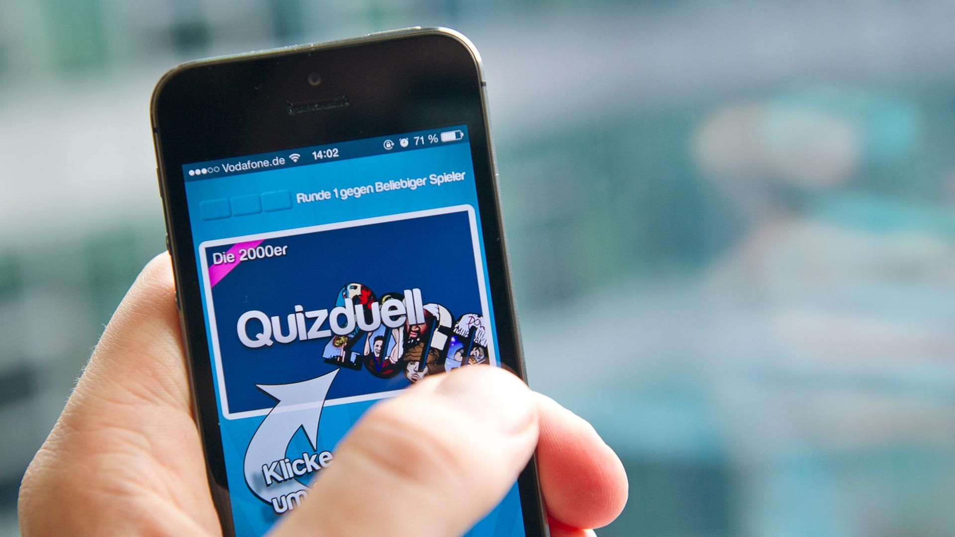 Eine Hand hält ein Smartphone, auf dem die Quizduell-App geöffnet ist. Eine Hand hält ein Smartphone, auf dem die Quizduell-App geöffnet ist.