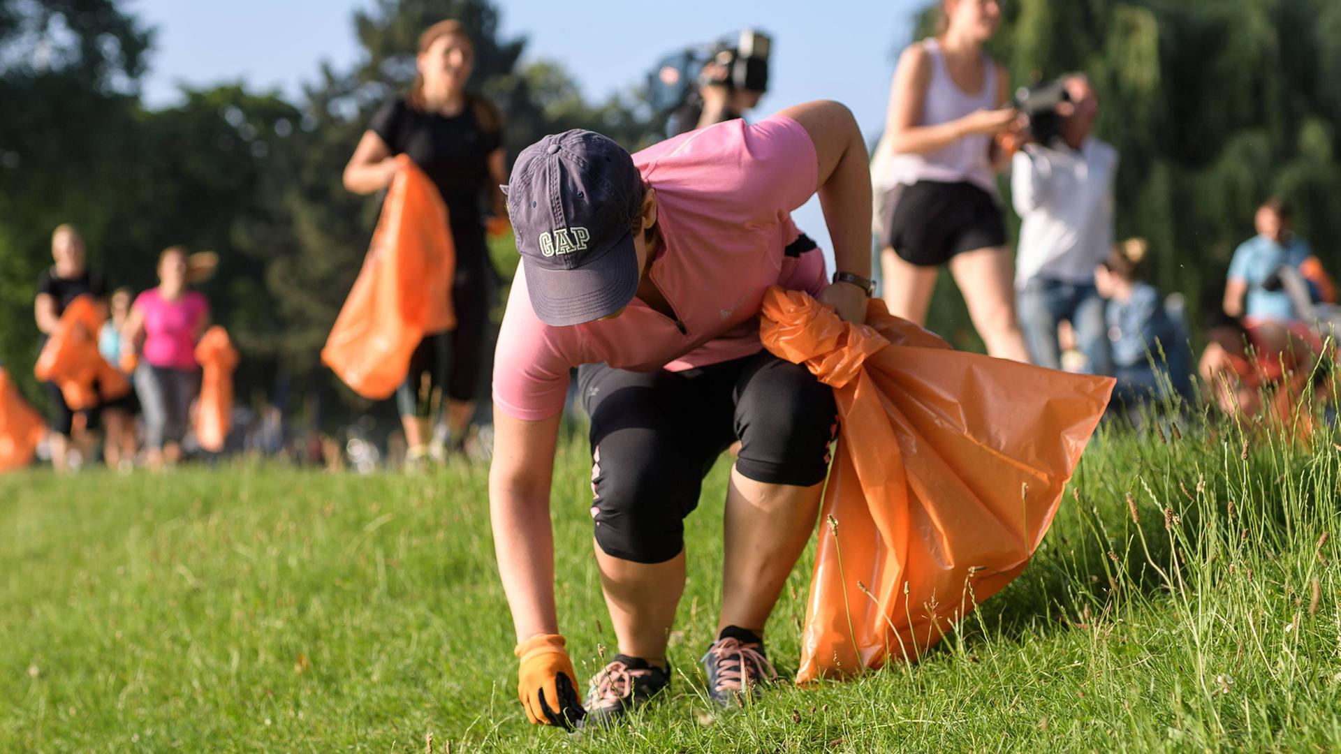 Plogging Lauf in Köln am Weltumwelttag am 5. Juni 2018 sammeln Müll in einem Park in orangenen Plastiktüten