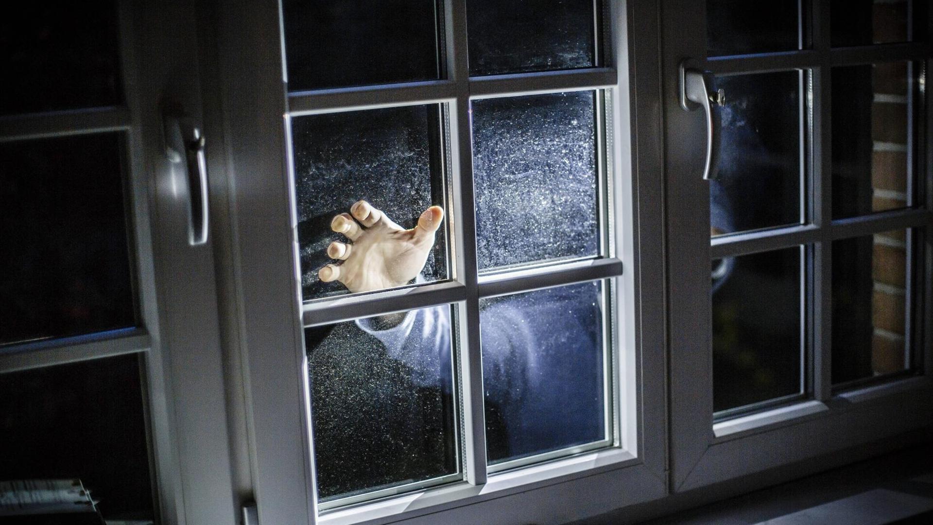 In einer gespielten Szene leuchtet ein Einbrecher durch ein Fenster
