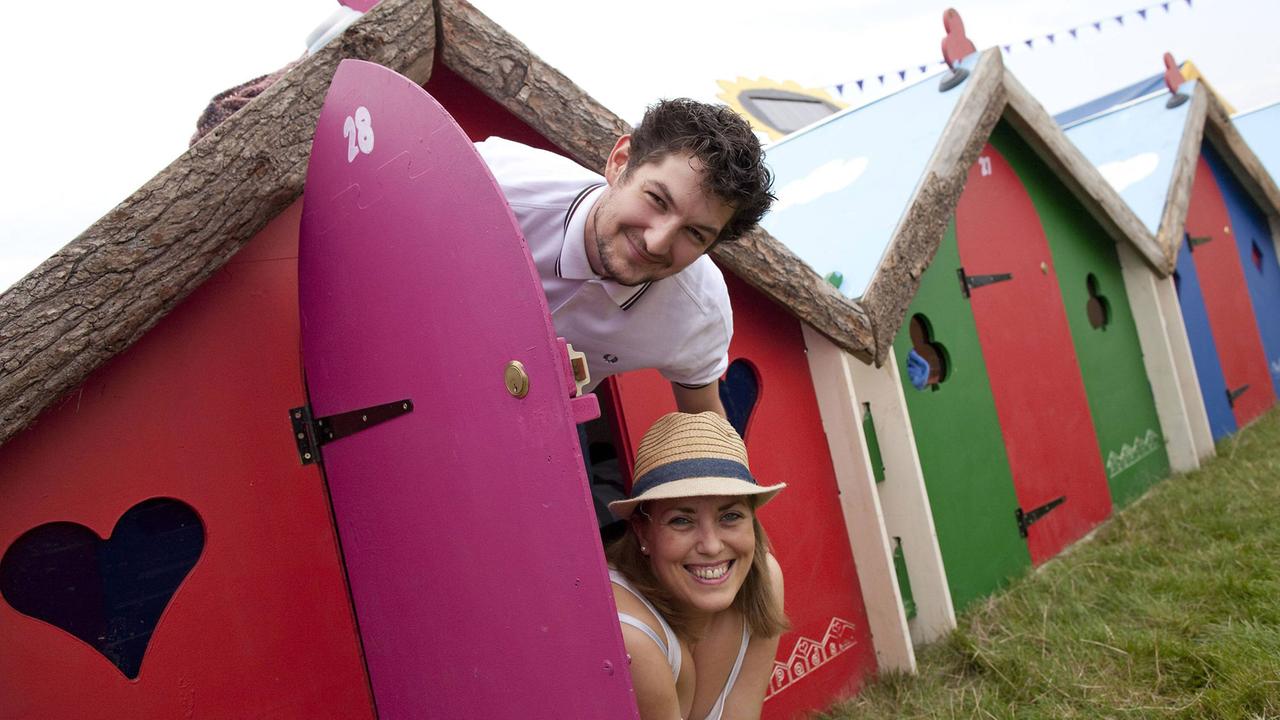 Zwei Besucher eines Festivals schauen lachend aus einem sogenannten Podpad heraus, einem bunten Minihaus aus Holz.