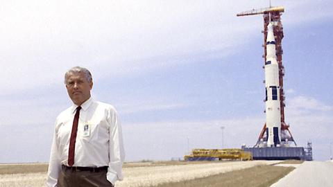 Wernher von Braun (1912-1977) am 1. Juli 1969 auf einem freien Feld, im Hintergrund eine Rakete in ihrem Startgestell.
