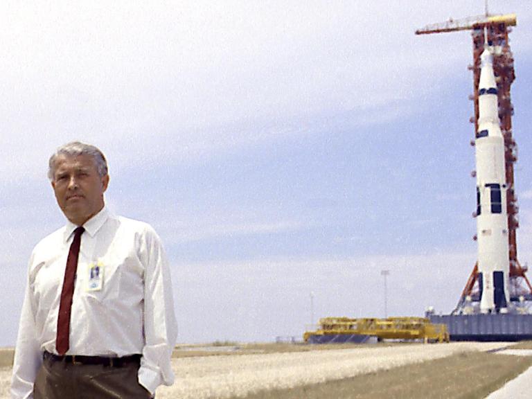 Wernher von Braun (1912-1977) am 1. Juli 1969 auf einem freien Feld, im Hintergrund eine Rakete in ihrem Startgestell.