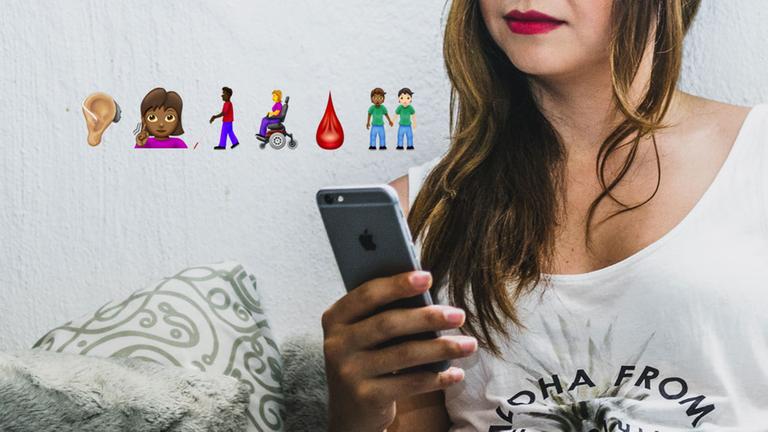 Eine Frau blickt auf ihr Smartphone, darüber sind einige der neuen Emoji 12.0 eingeblendet (Hörgerät, taube Frau, Blinder mit stock, Frau im Rollstuhl, Blutstropfen, zwei Männer, die Händchen halten).