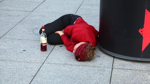 Eine junge Frau liegt völlig betrunken auf dem Pflaster an einer Plakatsäule
