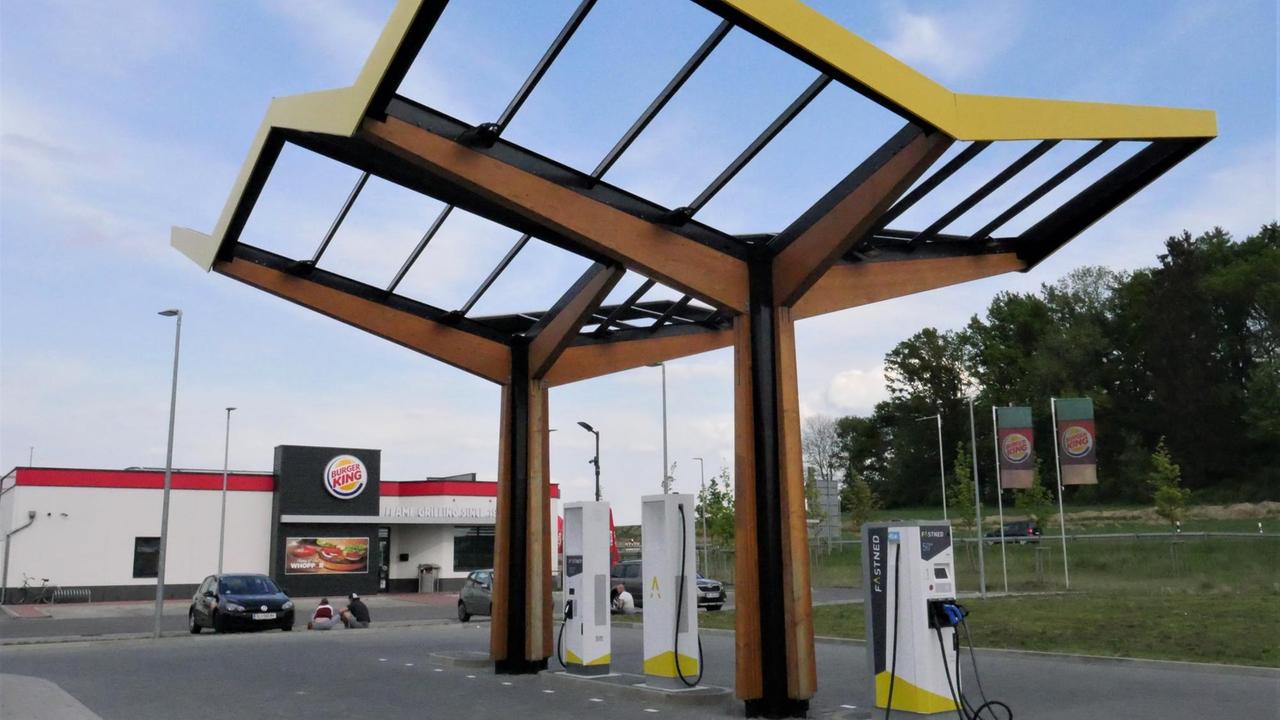 Eine E-Tankstelle mit Holz-Glasdach, im Hintergrund ein "Burger King"-Restaurant.