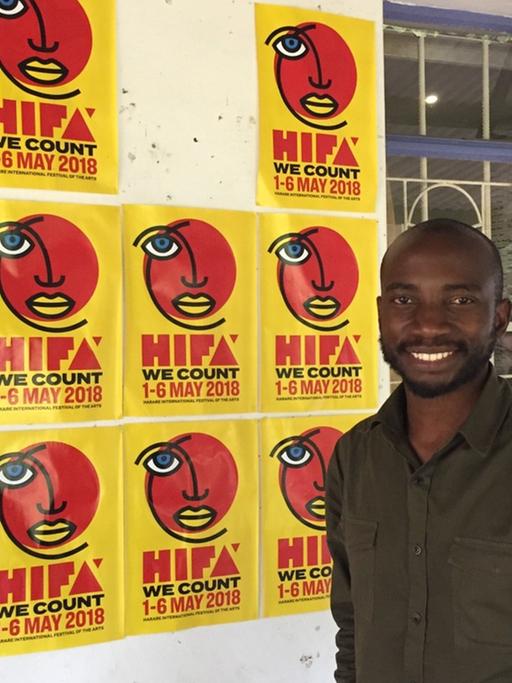 Tafadzwa Simba, stellvertretender Direktor des Hifa Festivals, steht in Simbabwes Hauptstadt Harare vor einer Häuserwand,die mit Plakaten zum Kulturfestival beklebt ist.