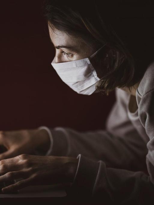 Eine Frau sitzt mit Atemschutzmaske vor ihrem Laptop.