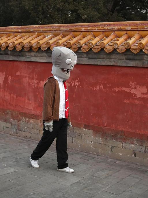 Ein chinesischer Schauspieler geht, als Zombie verkleidet, an einer Tempelmauer entlang
