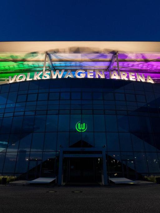 Das Stadion des VfL Wolfsburg erstrahlt vor einem dunklen Himmel in Regenbogenfarben.