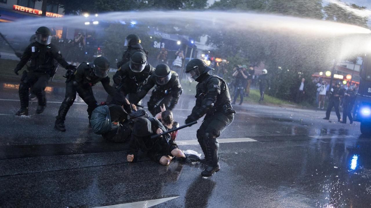 Ein Polizist schlägt mit einem Schlagstock auf Demonstranten beim G20-Gipfel 2017 in Hamburg ein, andere Polizisten halten die Protestierenden fest