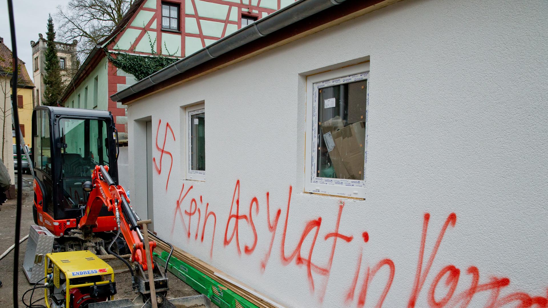 Eine frisch verputzte Hauswand mit dem in rot aufgesprühten Satz "Kein Asylat in Vorra" und einem Hakenkreuz.