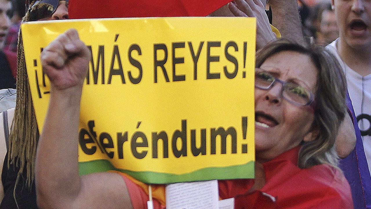 Menschen demonstrieren auf Spaniens Straßen. In der Mitte steht eine Frau mit einer Fahne um den Körper geschlungen und einem Plakat in der Hand, auf dem "Referendum" steht.