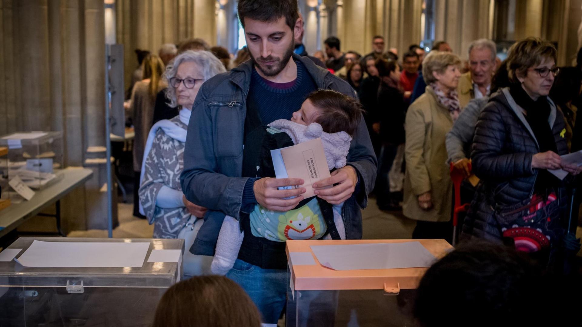 Ein spanischer Wähler mit Baby im Arm an einer Wahlurne.