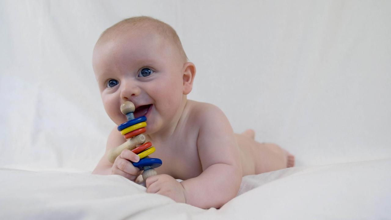 Baby, auf dem Bauch liegend, mit Rassel 