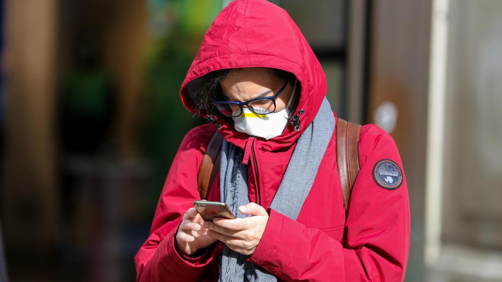 Ein Mann in London mit einer Schutzmaske am 11. März 2020 blickt auf sein Smartphone.
