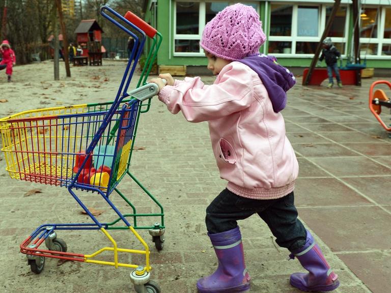Ein Kind schiebt einen Kinder-Einkaufswagen über einen Spielplatz.