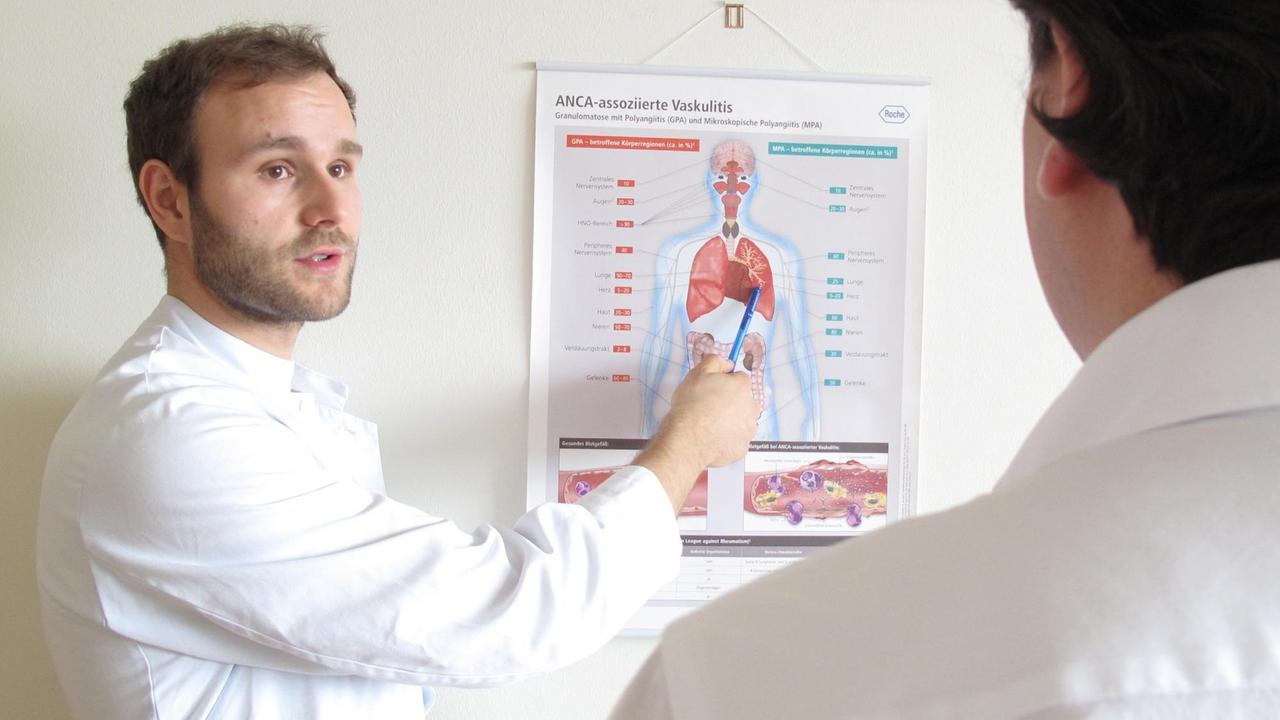 Ein Artzt im weissen Kittel erläutert einem Patienten, den man nur von hinten sieht, das, was auf einer medizinischen Tafel erläutert ist.