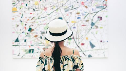 Eine Frau betrachtet ein Gemälde in einer Ausstellung, ihr sommerliches Oberteil und das Bild haben ein ähnliches Muster.