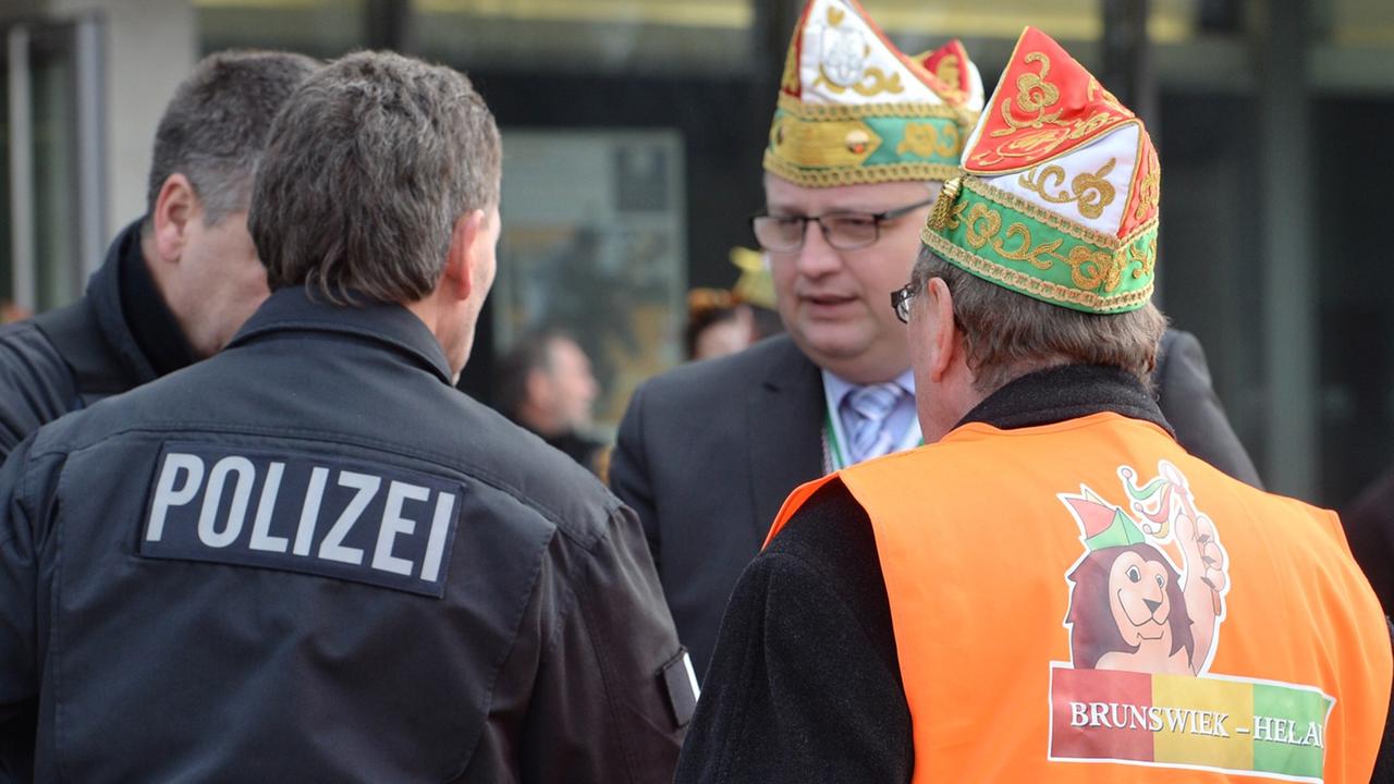 Polizisten und ein Karnevalist mit Narren-Mütze auf einer Straße in Braunschweig Polizisten und ein Karnevalist mit Narren-Mütze auf einer Straße in Braunschweig