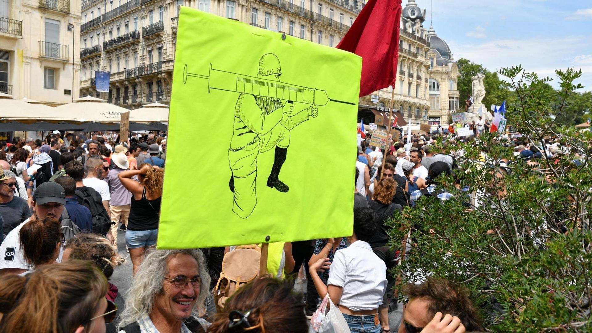 Protestierende in Marseille halten ein grünes Plakat mit einer Zeichnung in die Höhe. Darauf ein Mann, der eine Impfspritze wie eine Waffe hält.