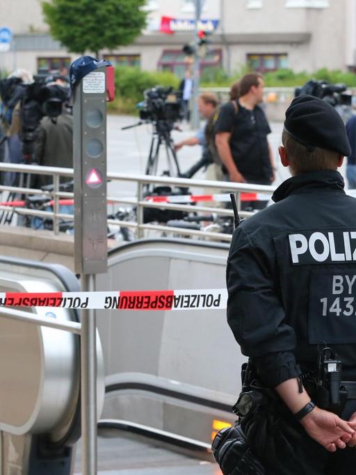 Sie sehen Polizisten und ein Absperrband am Eingang zur U-Bahnstation Olympia-Einkaufszentrum.